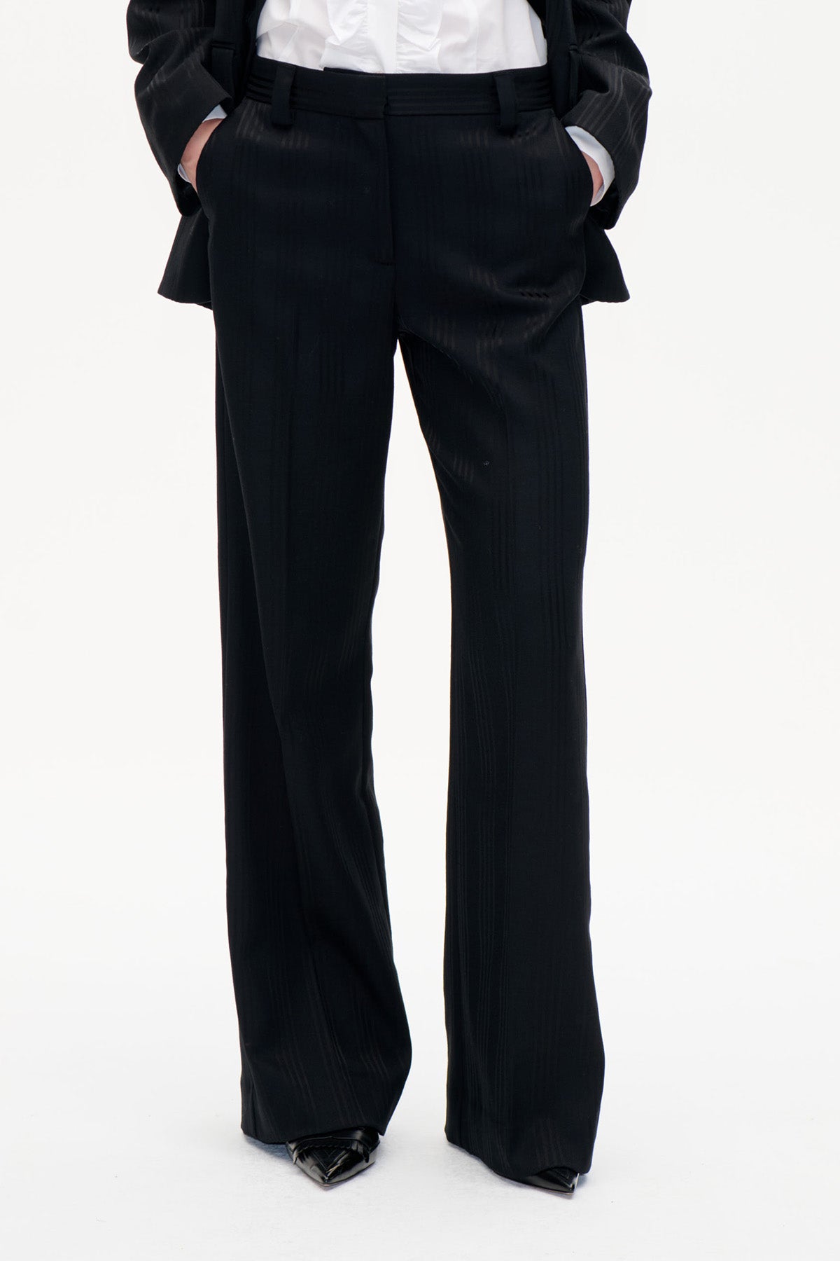 Front view of black wide-leg trousers with subtle vertical stripes and a high waistband, styled with a white shirt and black jacket.