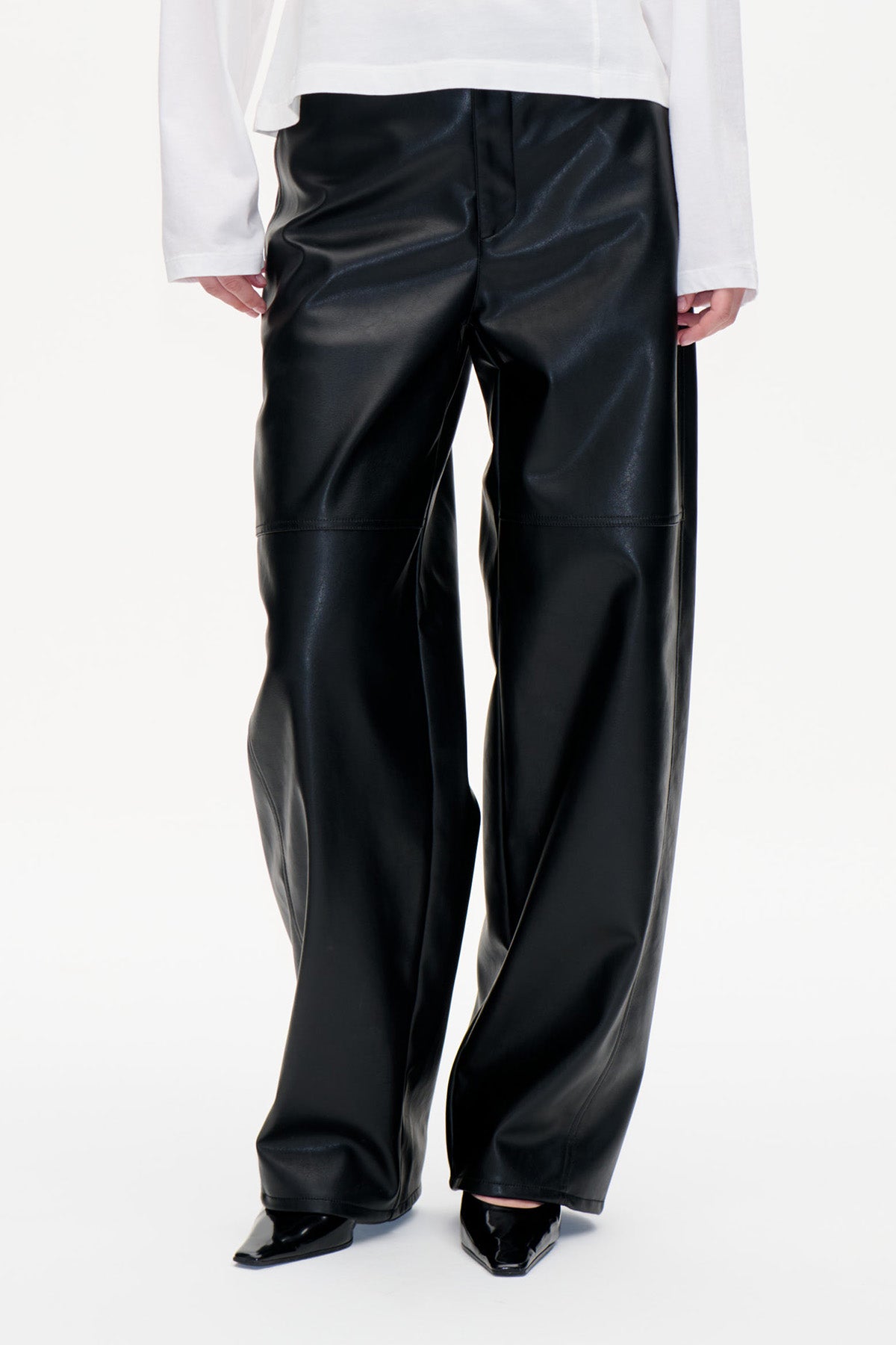 Front detail of glossy black wide-leg trousers with horizontal knee seams, styled with a white long-sleeved top.