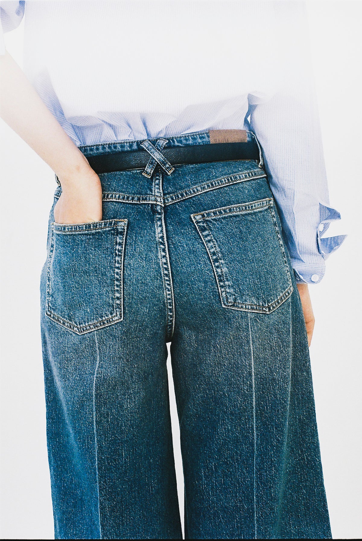 Close-up rear view of blue wide-leg jeans with two patch pockets and a light blue striped shirt tucked into the waistband