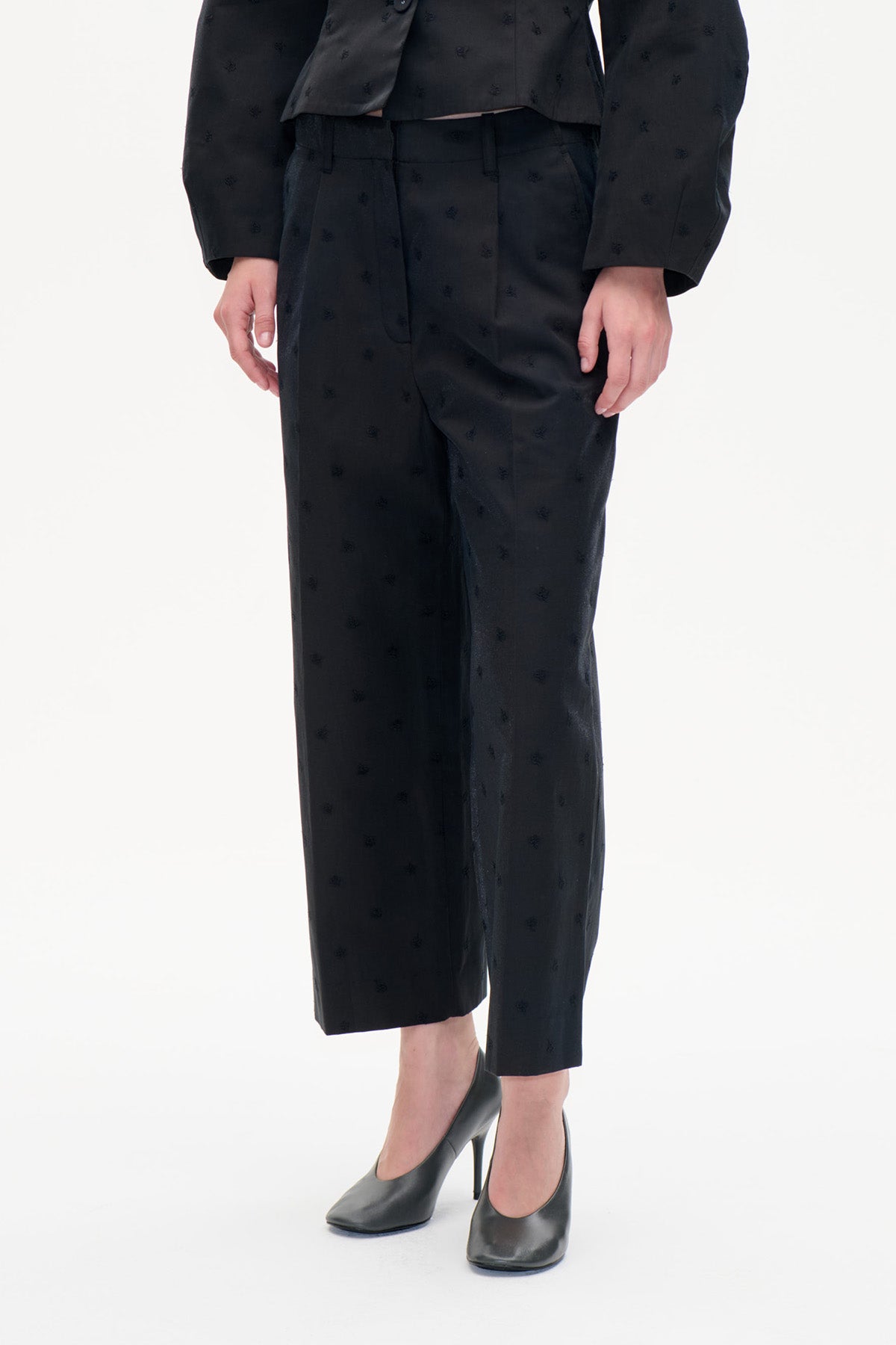 Vooraanzicht van zwarte, getailleerde broek met subtiel ton-sur-ton-motief en rechte enkellange pijpen.