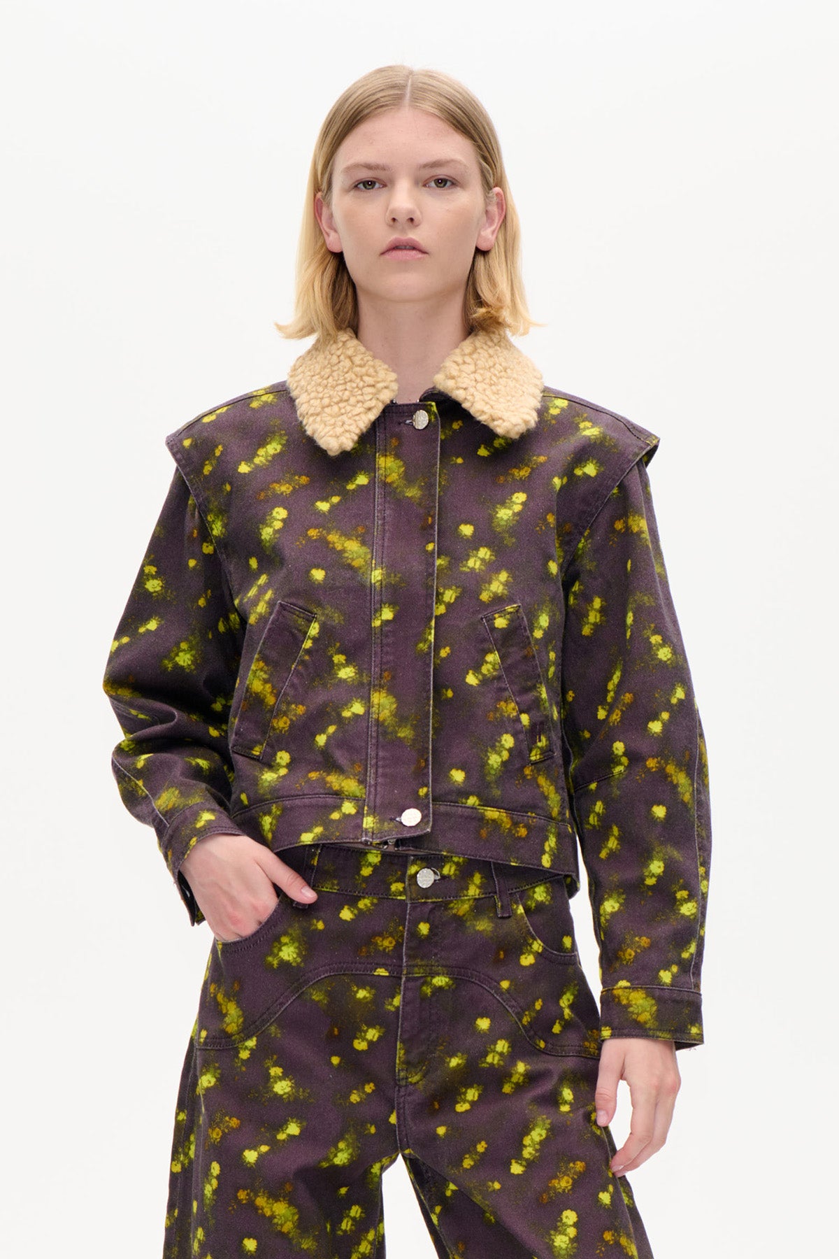 Front view of a cropped dark plum jacket with bright yellow mottled pattern, cream shearling-style collar and snap buttons, worn with matching trousers.