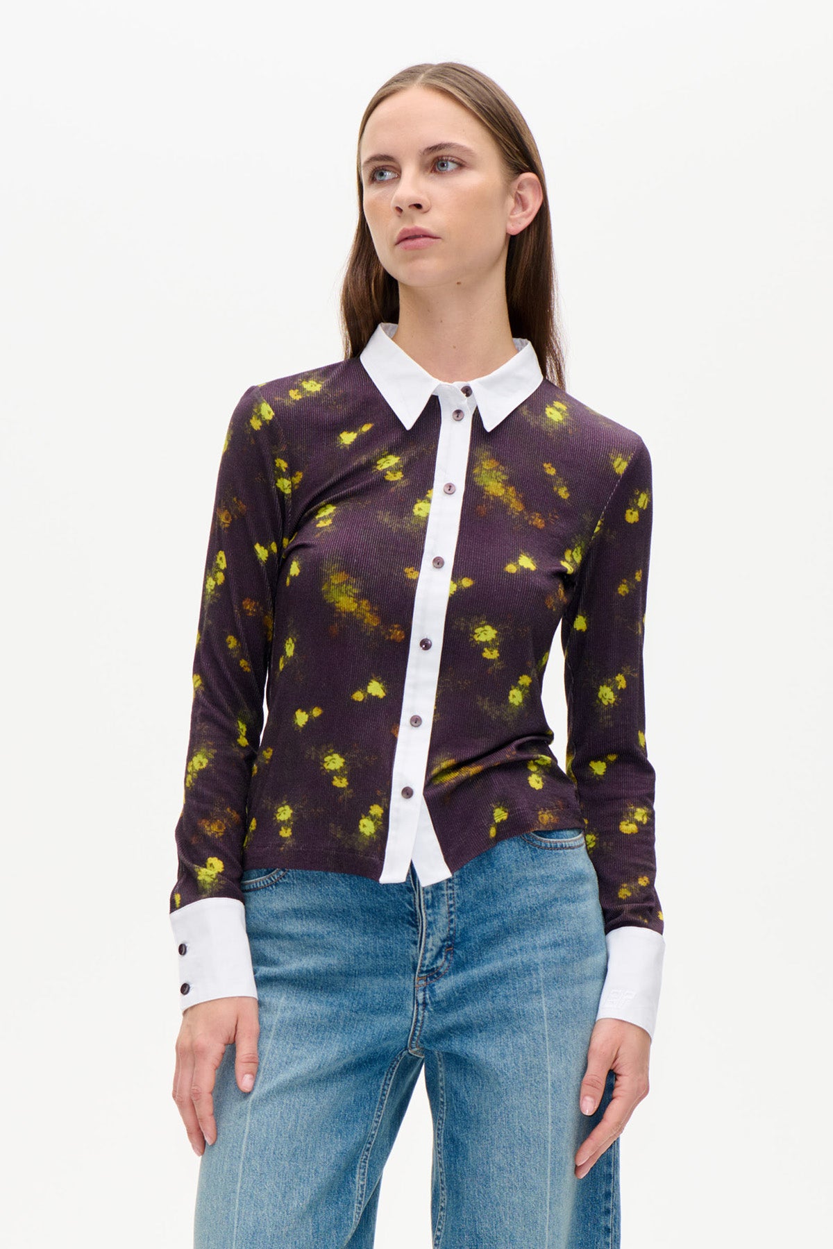 Vorderansicht eines dunkelpflaumenfarbenen, geblümten Cardigans mit Knopfleiste, leuchtend gelb-grünen Blumen, weißem Kragen und Bündchen, kombiniert mit blauen Jeans.