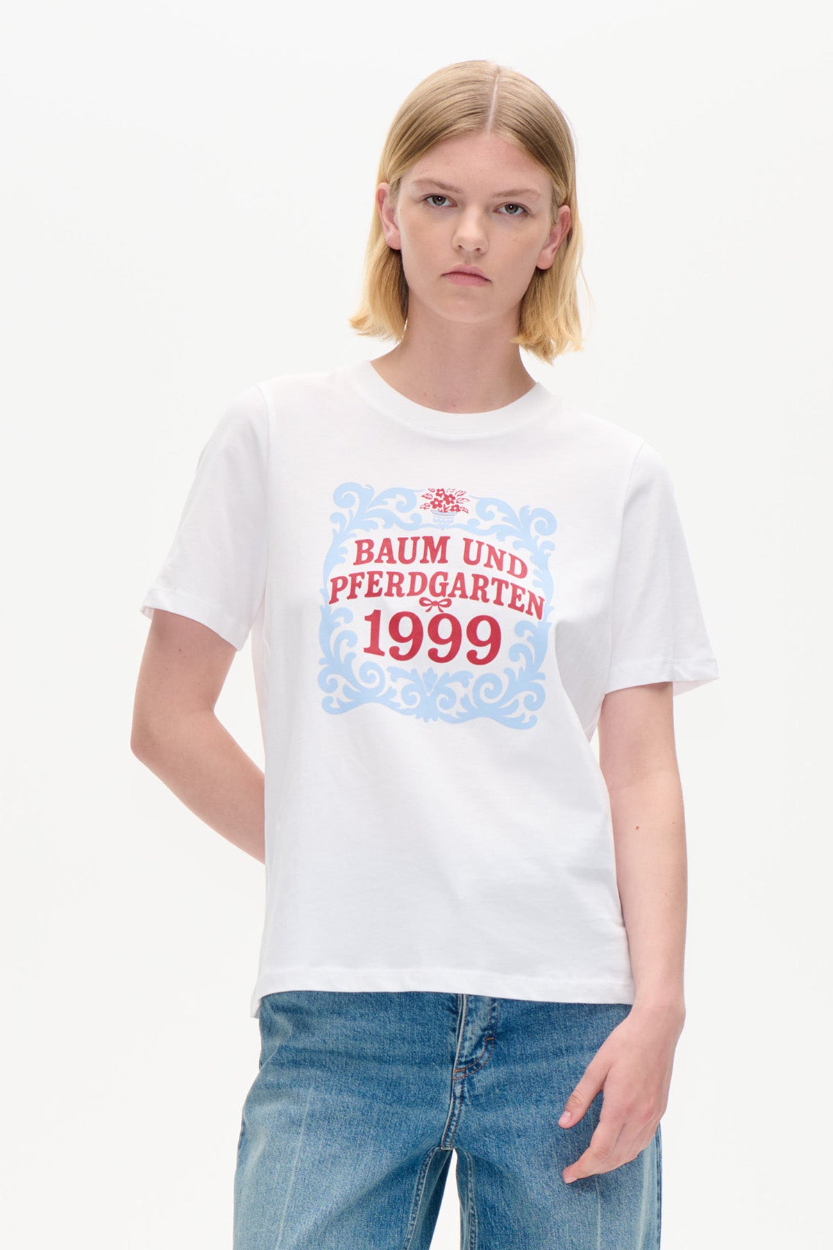 White short-sleeved T-shirt with a blue ornamental frame and red Baum und Pferdgarten 1999 graphic, shown from the front.