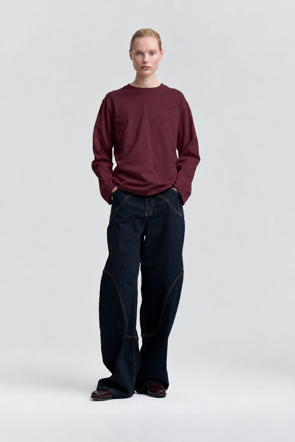Front view of a model wearing a burgundy long-sleeve sweatshirt and wide-leg dark indigo jeans with contrast stitching.
