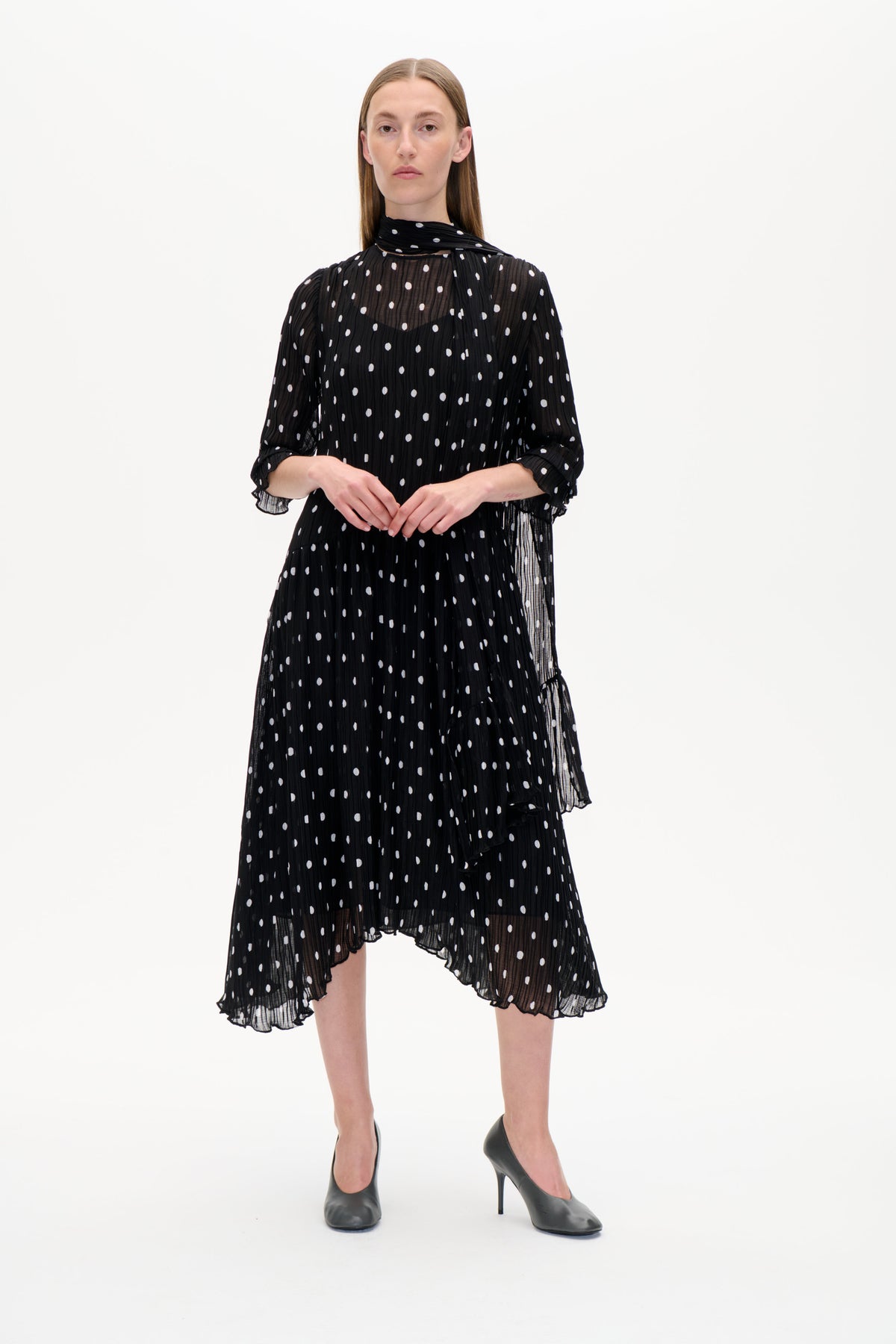 Front view of a black sheer dress with white polka dots, a scarf-style neckline, long sleeves and a ruffled hem.