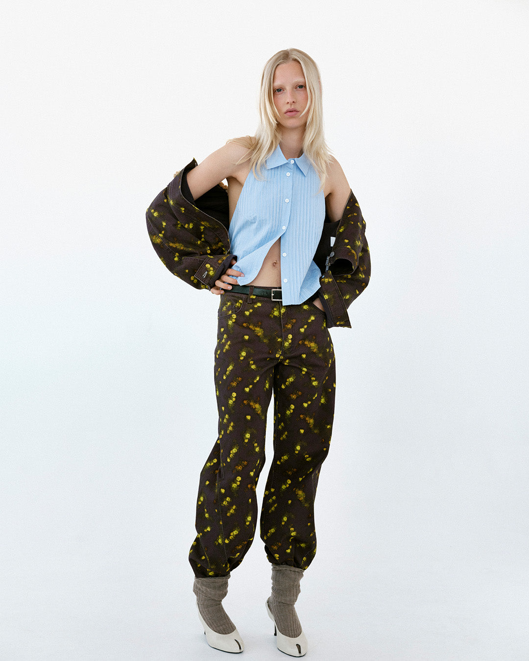 Ganzkörper-Fashion-Porträt: ärmellose, hellblaue Bluse mit Knopfleiste, dunkelbrauner Blazer und passende Hose im gelben Sprenkelmuster.