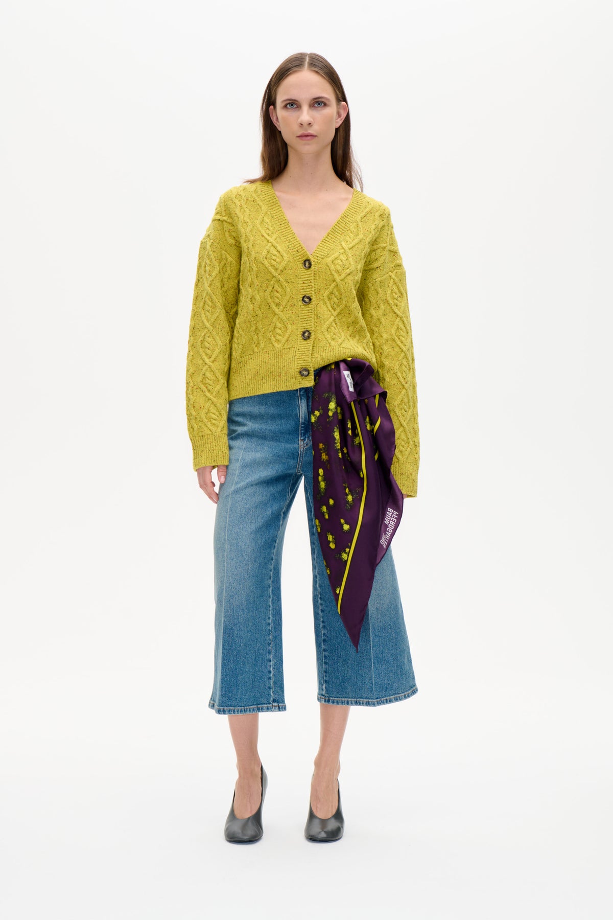 Front view of a model wearing a yellow-green cable-knit button cardigan with blue wide-leg jeans and a purple floral scarf.