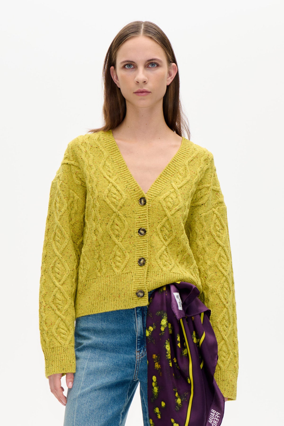 Front view of a lime-yellow cable-knit cardigan with a V-neck, long sleeves and dark buttons, styled with blue jeans.