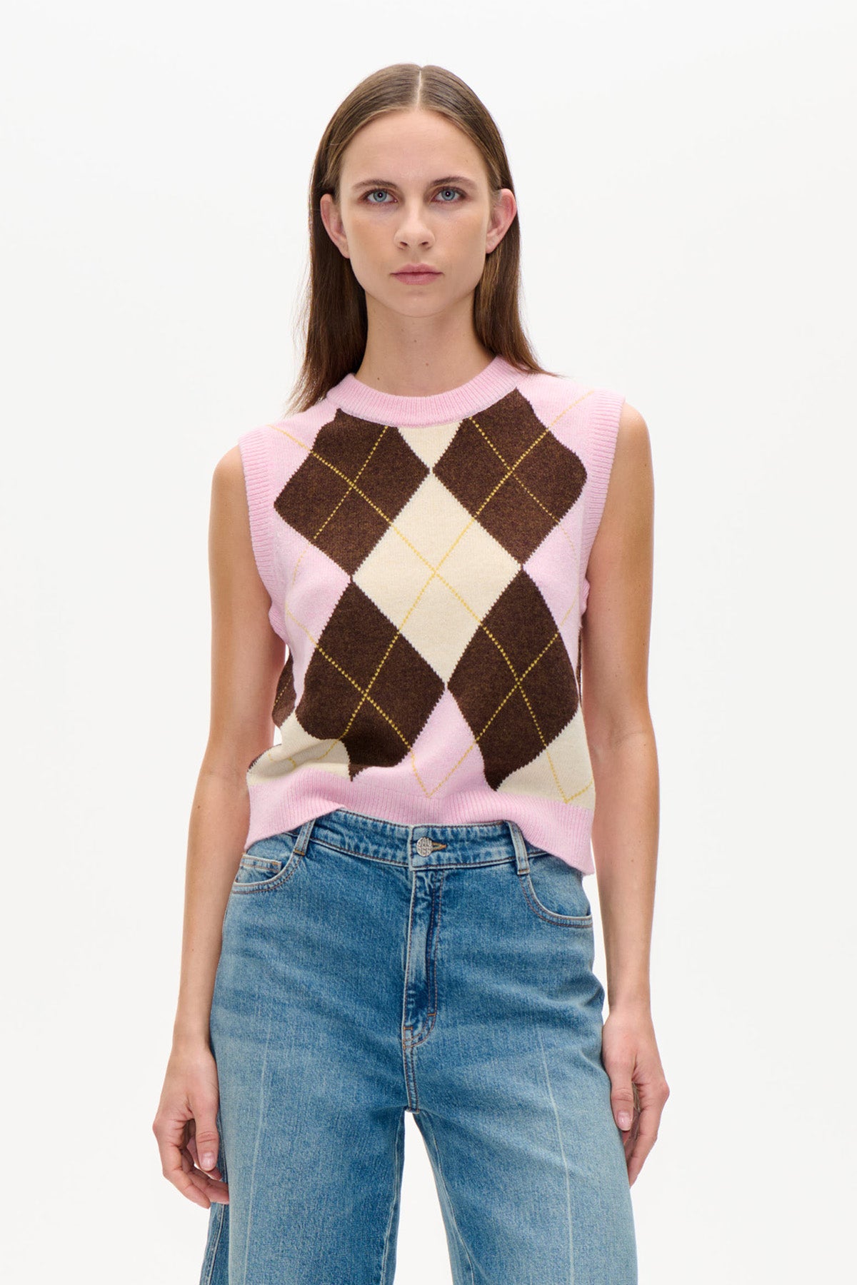Front view of a pink sleeveless knitted vest with cream and dark brown argyle diamonds, worn with blue jeans.
