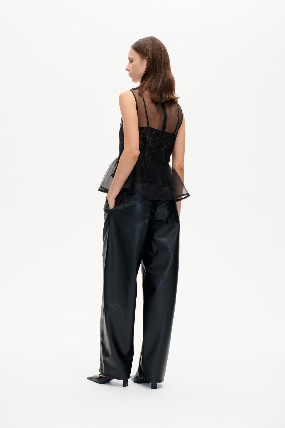 Model in a black sheer sleeveless top with vertical trim and a lace panel, paired with wide-leg black trousers, shown from behind.