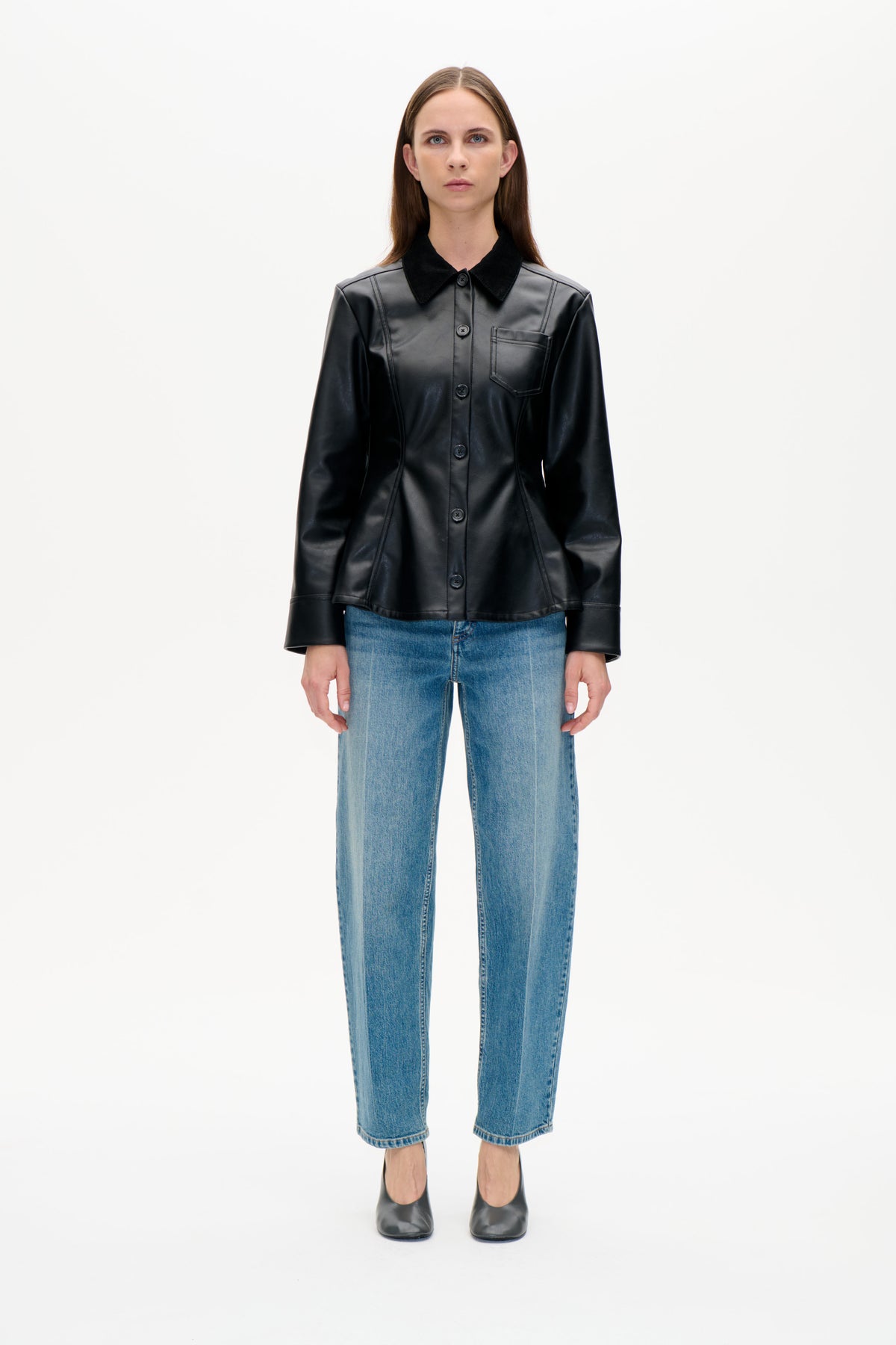Vorderansicht eines Models, das eine schwarze Jacke mit Knopfleiste, kontrastierendem Kragen und Brusttasche sowie blaue Jeans und schwarze Schuhe trägt.