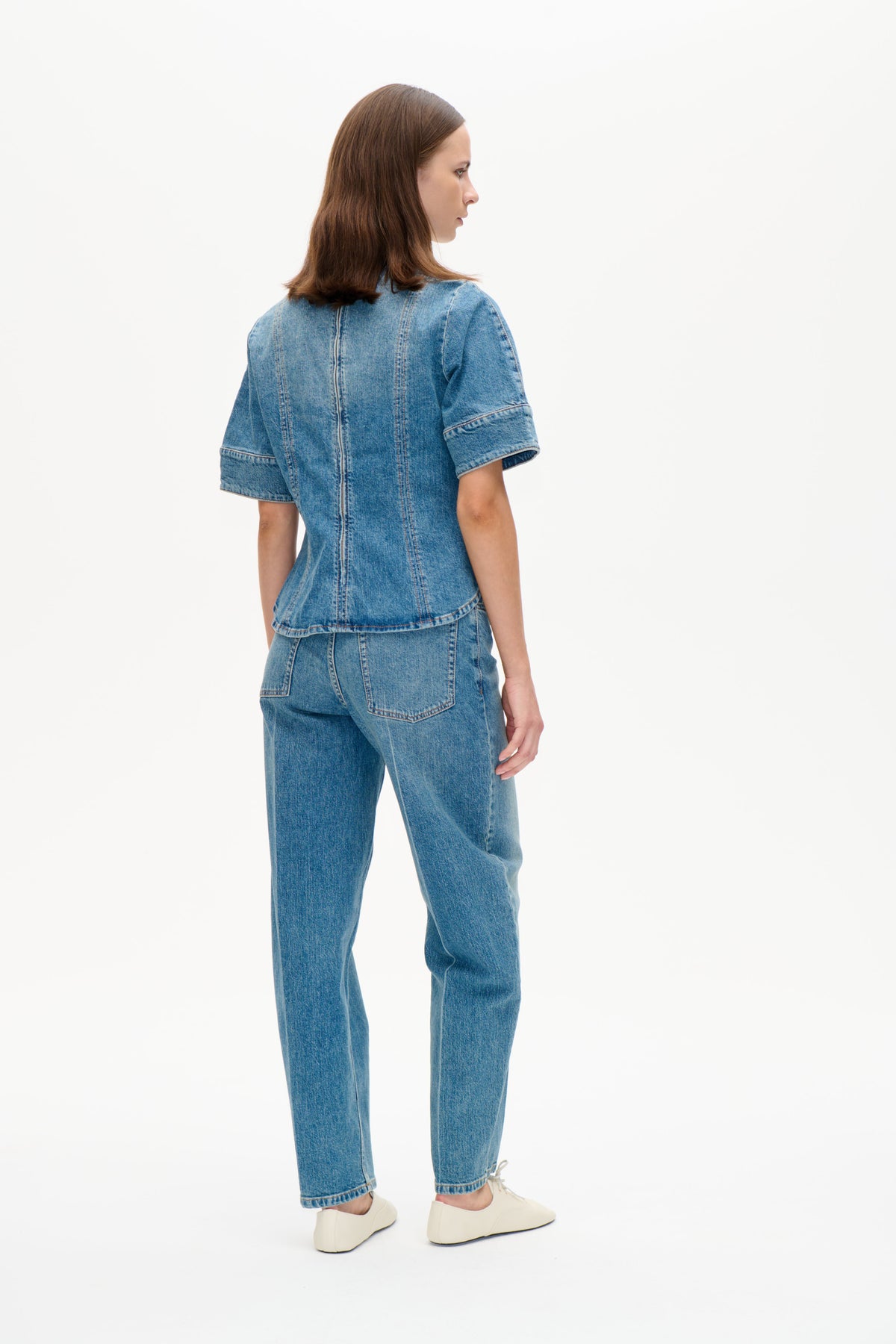 Model in a blue denim short-sleeved top and matching jeans, shown from the back and side against a white background.