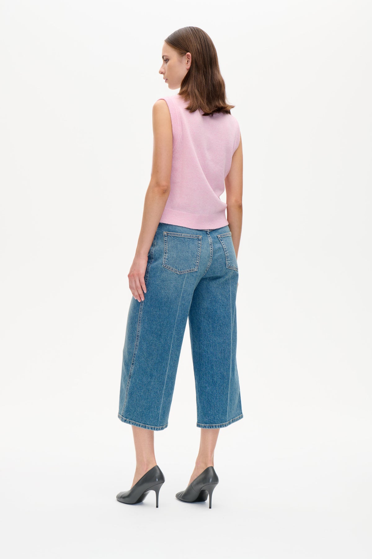 Model in a pale pink sleeveless knit vest and blue wide-leg cropped jeans, shown from the side and back.