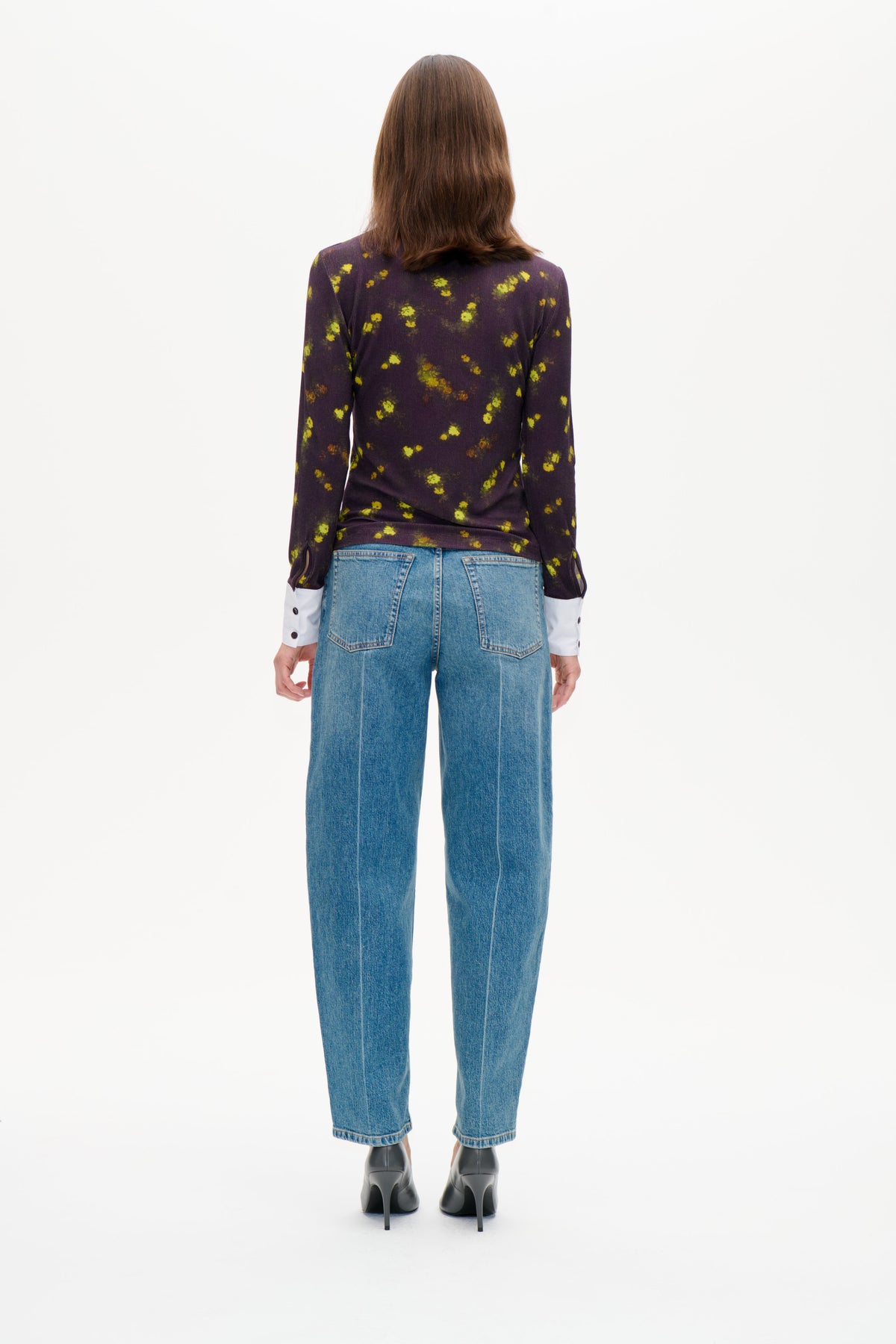Vue de dos d'un mannequin portant un haut à manches longues violet foncé à imprimé floral jaune-vert épars, superposé à des poignets blancs et associé à un jean bleu