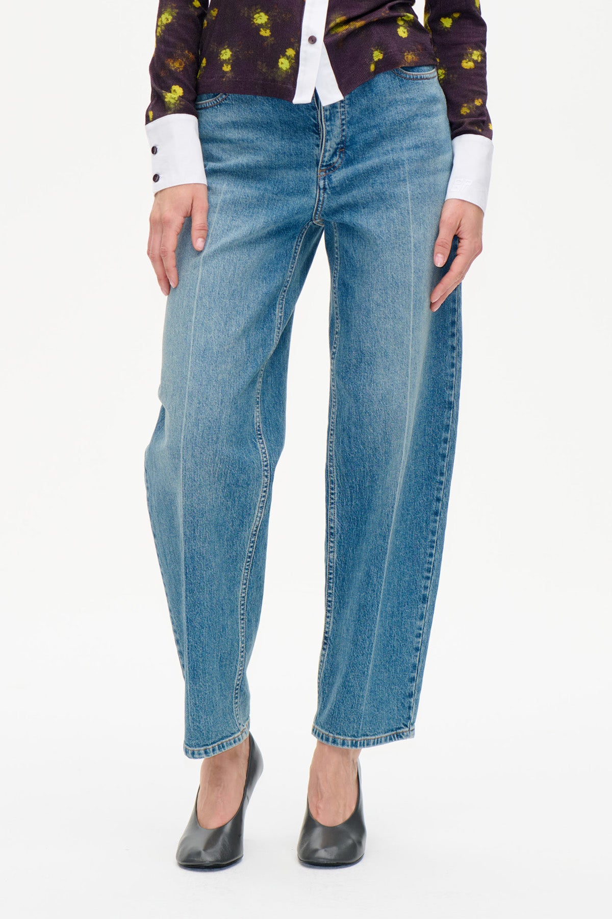Détail avant d'un jean droit bleu à effet délavé, associé à un top floral foncé et des escarpins noirs.