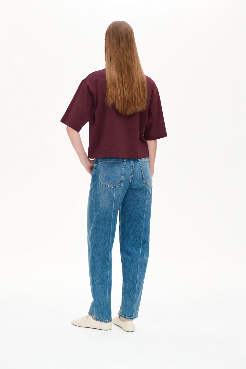 Back view of a model wearing a burgundy cropped T-shirt and blue jeans with a subtle tonal pattern and patch pockets.