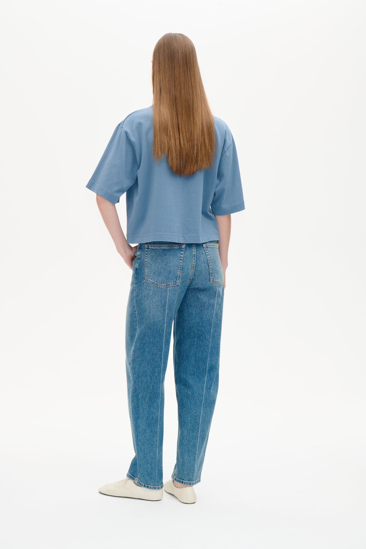 Back view of a model wearing a relaxed blue short-sleeved T-shirt with medium-wash blue jeans.
