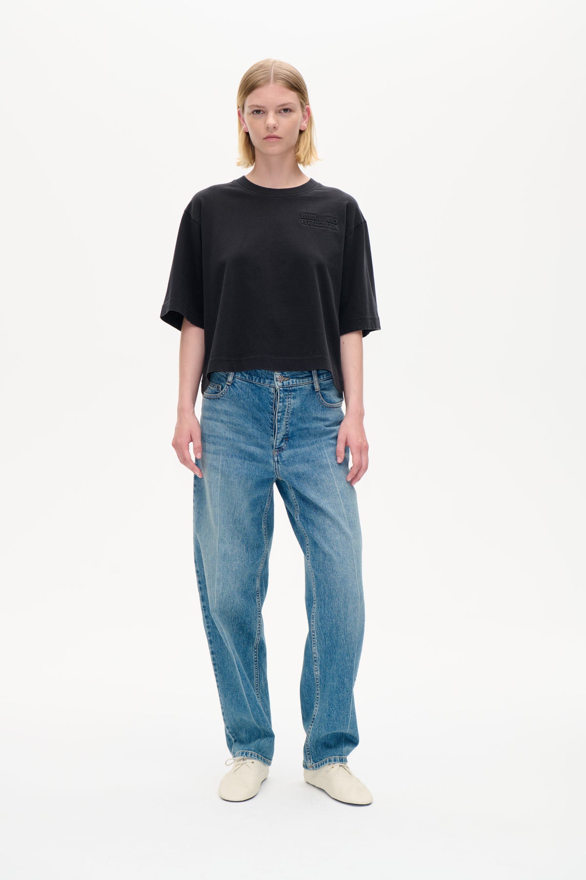 Vorderansicht eines Models, das ein oversized anthrazitfarbenes T-Shirt mit Ton-in-Ton-Baum und Pferdgarten-Schriftzug auf der Brust und eine blaue Jeans trägt.