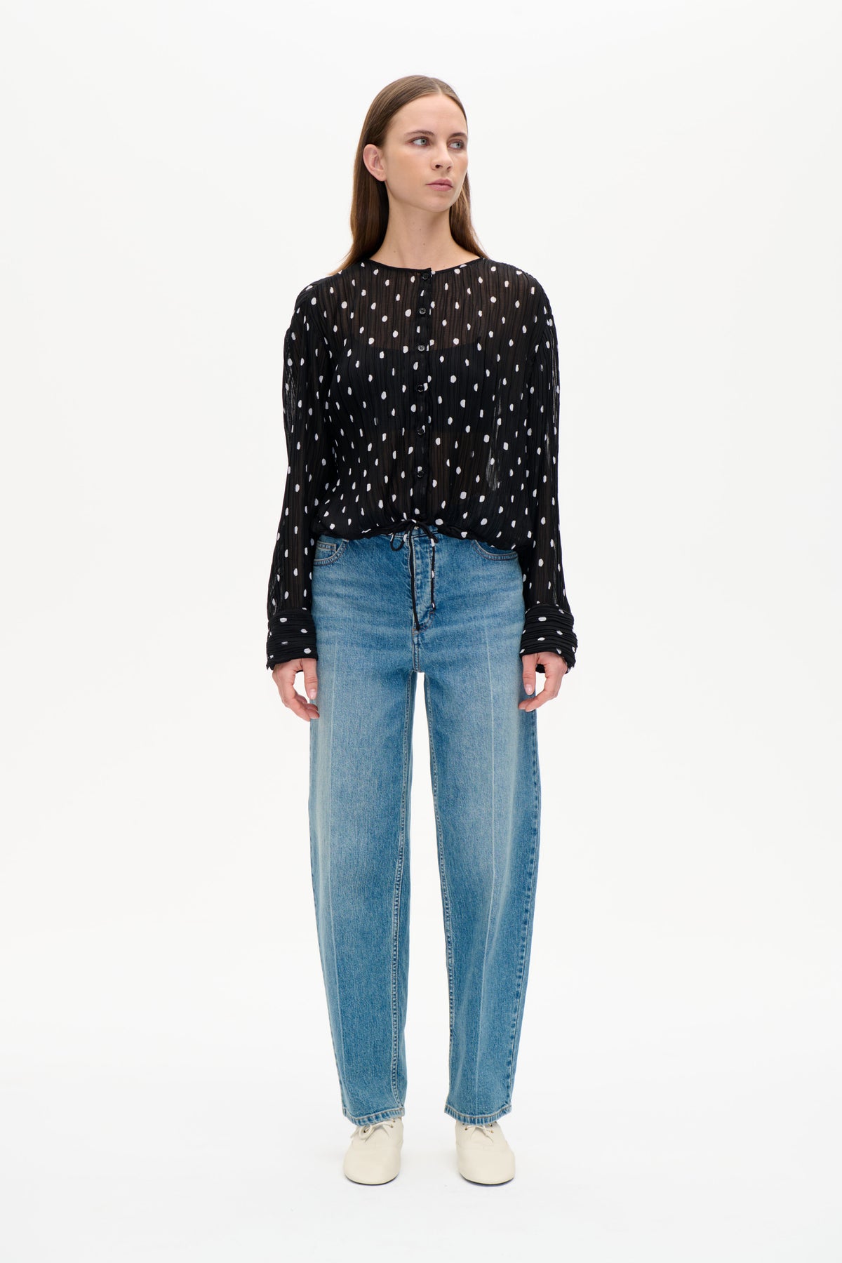 Front view of a black sheer, crinkled blouse with scattered white dots, button front, long sleeves and drawstring hem.