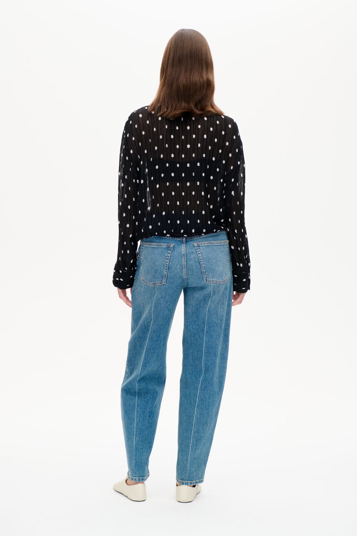 Back view of a black sheer long-sleeved blouse with white polka dots, worn with blue jeans.