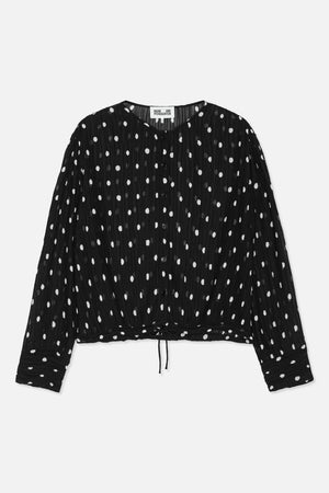 Front view of a black long-sleeved button-front blouse with white polka dots, a V-neck and adjustable drawstring hem.