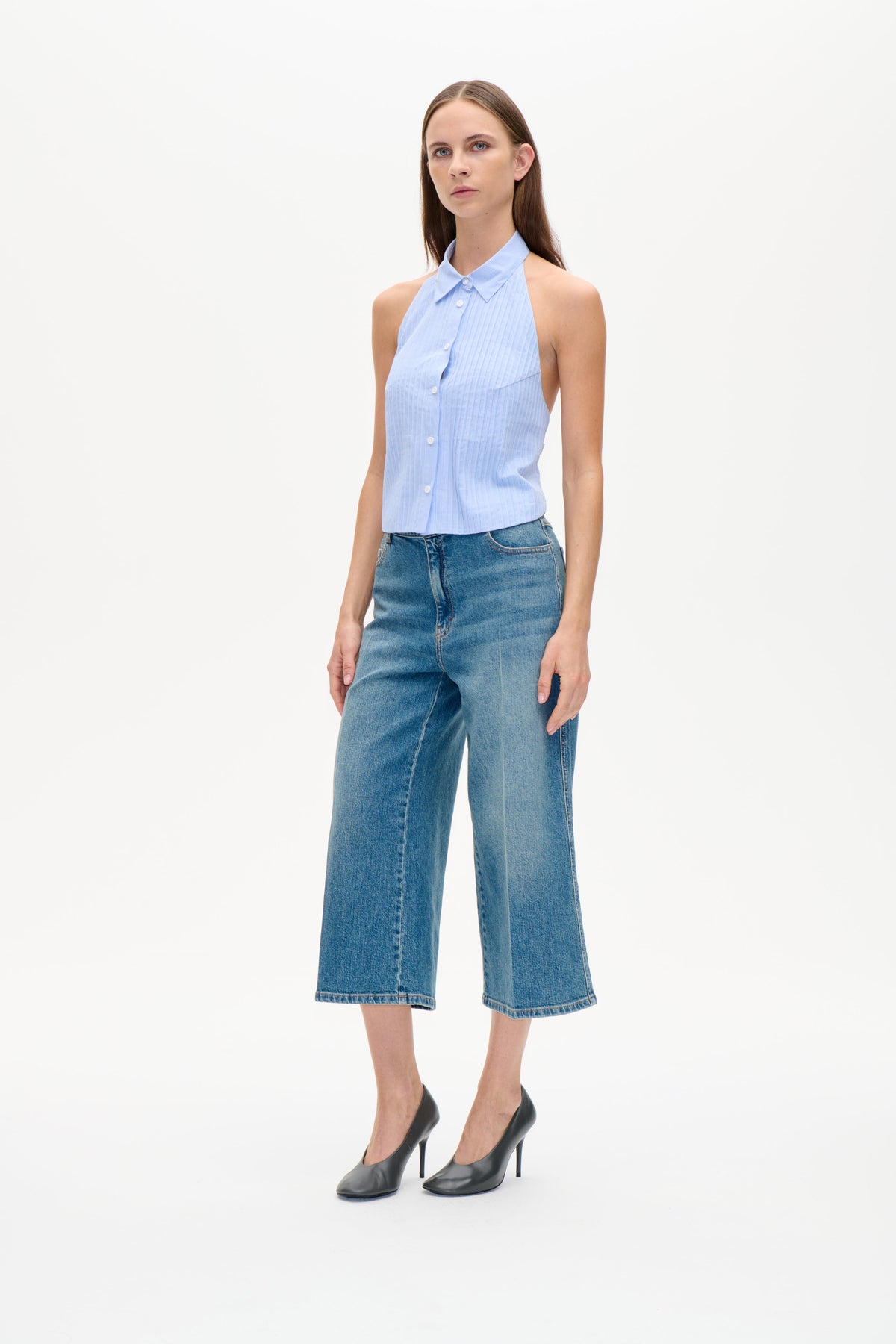 Model trägt ein hellblaues, fein gestreiftes, ärmelloses Top mit Knopfleiste und spitzem Kragen sowie eine weit geschnittene blaue Jeans.