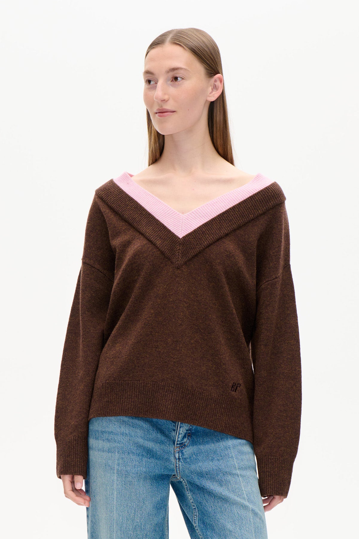 Front view of a dark brown sweater with a wide off-shoulder V-neck trimmed in pink ribbing, worn with blue jeans.