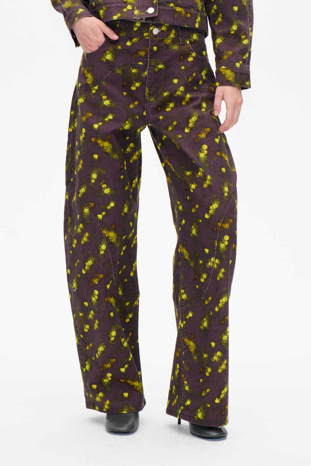 Front detail of wide-leg dark plum trousers with bright yellow-green splatter print and curved panel seams.