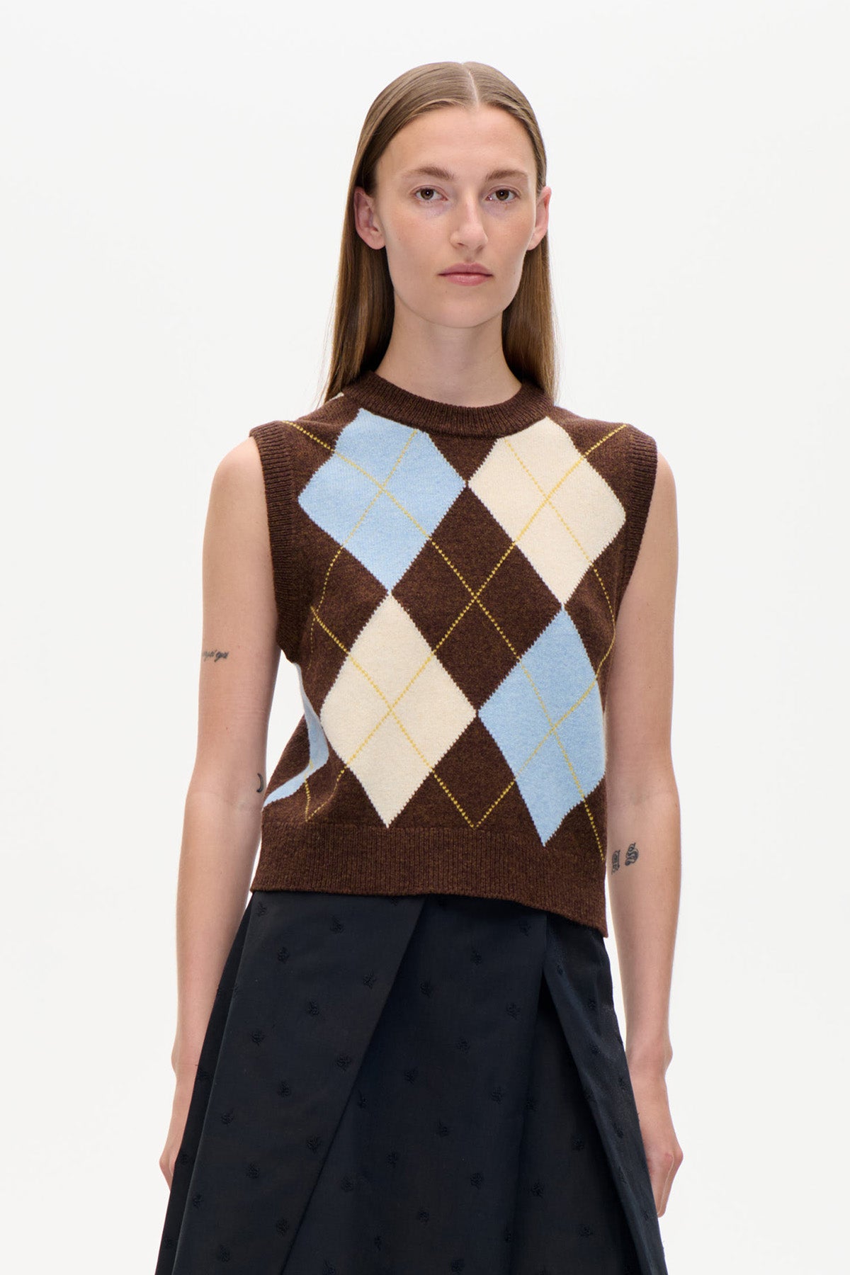 Front view of a sleeveless brown knit vest with large pale blue and cream argyle diamonds, worn with a black skirt.