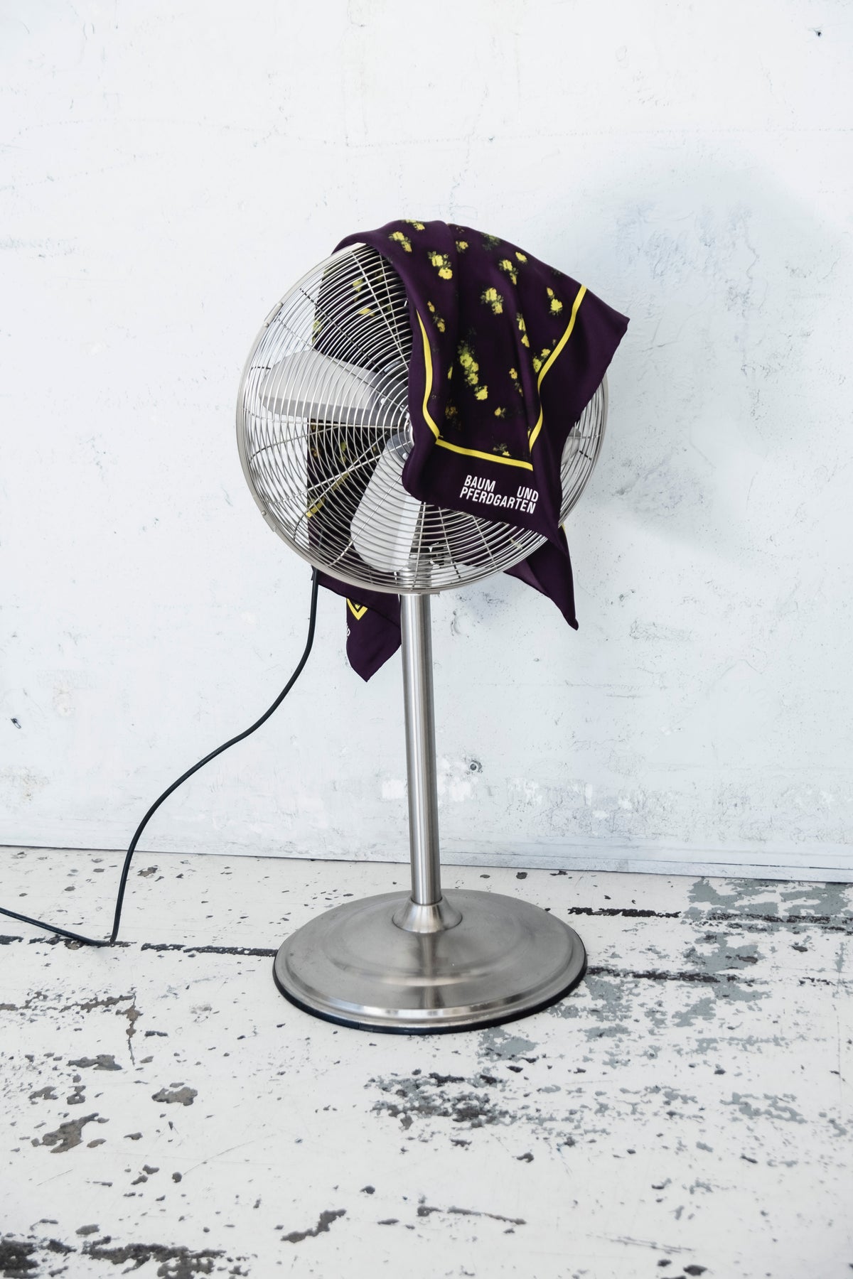 A purple garment with yellow floral motifs and piping draped over a metal fan, with Baum und Pferdgarten lettering.